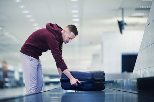 Traveling by airplane. Passenger pick up his blue suitcase in baggage claim in airport terminal..