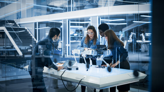 Diverse Colleagues Work in Industrial Robotics Factory, Experimenting With a Mobile Robot Prototype. Scientists Use Computers to Program the Robot Dog Before Development Testing.