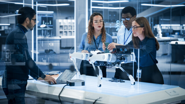 Professional Multicultural Team of Female and Male Engineers Use Industrial Programmable Robot Dog in a Factory Development Workshop. Tech Facility with Machines, Computers and Research Equipment.