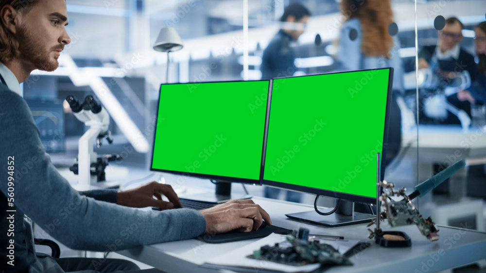 Fototapete Software Developer Working on Computer with Green Screen Mock Up Display. Scientific Lab, Engineering Research Center with Specialists Working on Mobile Robot Development in the Background.