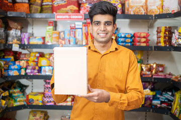 Young Indian man showing blank white box at grocery store or supermarket, Product mockup.