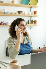 Obraz premium Female ceramist reading a text message on her smartphone. Creative businesswoman managing a store with a collection of ceramic products. Young entrepreneur running a successful small business