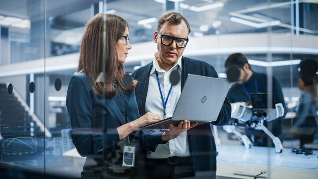 Chief Robotics Engineer Having Meeting with Project Manager and Machinery Operators Next to a Mobile Robot Animal Project. Young Team Using Computers, Discussing the Development of an AI Robotic Dog.