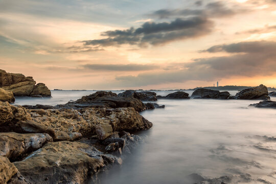Scenic view of rocks in sea against cloudy sky with Nojimasaki lighthouse in background