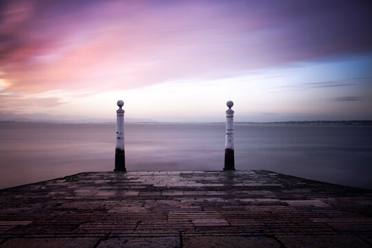 Scenic view of Cais das Colunas by Tagus River against cloudy sky at sunrise