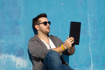 Side view of a young man with sunglasses sitting on stairs while using a tablet pc