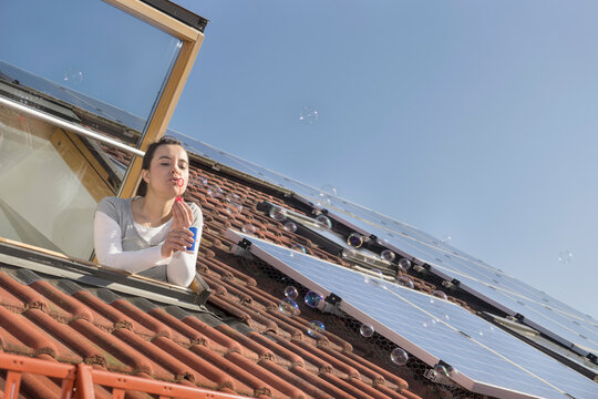 Woman blowing bubbles out of roof window with solar panels