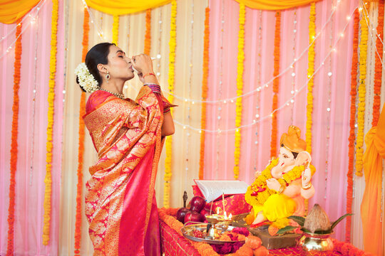 Image of an Indian woman in silk saree blowing shankh or a conch shell on festival puja/pooja: Diwali/Ganesh Chaturthi/Guru Purnima. Stock image of a married woman in saree blowing a conch shell (s...