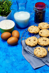 preparation chocolate cookies, eggs with flour bowl and milk bottle. coffee beans and empty plate above plaid napkin