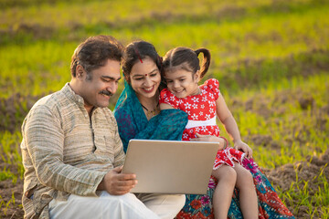 Indian farmer using laptop with wife and daughter at agriculture field.