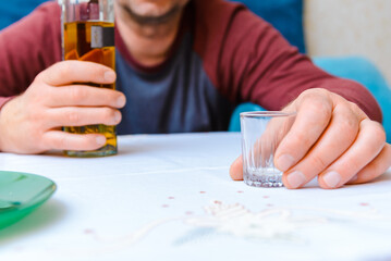 Uncontrolled consumption of alcohol,alcoholizm disease.Closeup of bottle of alcohol and glass.Concept of uncontrolled consumption of alcohol.Drunk man at home.