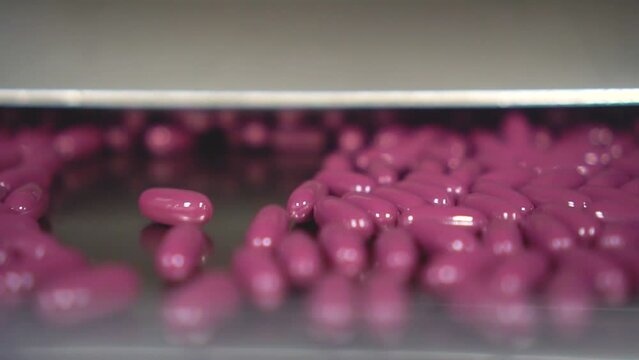 Cápsulas de color rosa saliendo de  la máquina de una industria farmacéutica.