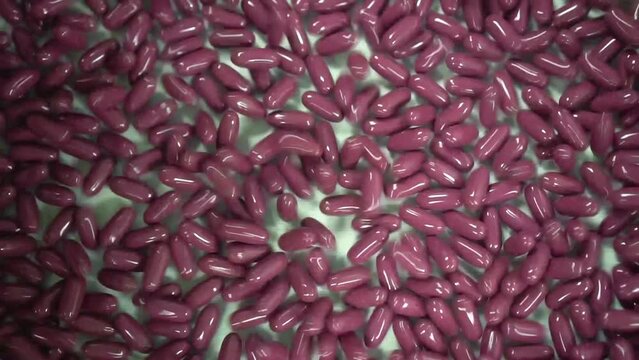 c&aacute;psulas rosas saltando y rebotando sobre cinta corredera blanca hacia la izquierda en empresa farmac&eacute;utica.