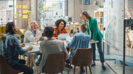 Female Chief Analyst Holds Meeting Presentation for a Team of Economists. She Shows a Whiteboard with Growth Analysis, Charts, Statistics and Data, Answers Questions. People Work in Creative Office