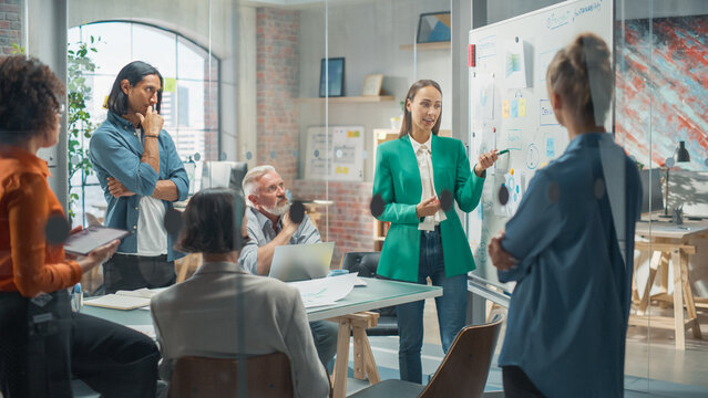 Female Project Manager Makes a Presentation for a Diverse Creative Team in Meeting Room in an Agency. Colleagues Gathering Around Conference Table and Discuss Business Development and Design.