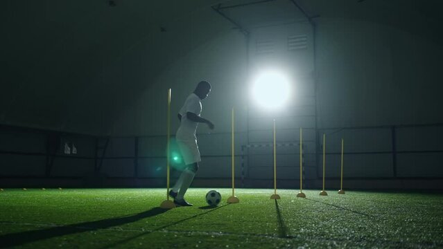 young football forward training in hall on artificial grass, practicing dribbling, slow motion