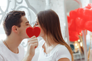 Two young people kissing behind a paper heart. Celebrating Saint Valentine's day. - obrazy, fototapety, plakaty