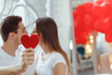 Cute couple in love kissing behind a paper heart with air balloons in shape of the heart....