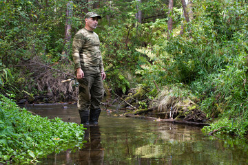 a fisherman with a spinning rod in his hand stands on a small forest river