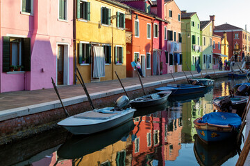 Burano, Venezia. Barche da pesca al palo in canale e case colorate con riflesso in acqua