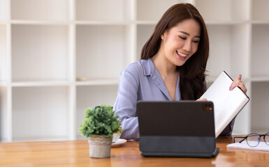 Portrait of a beautiful, young and intelligent-looking Asian woman student smiling as she works on her tablet in a university classroom.