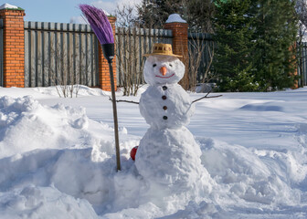  Snowman in a straw hat and a broom in his hand in a snowy garden.