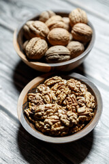 Peeled walnuts and nuts in a  shell in walnut wooden bowl on a wooden background.