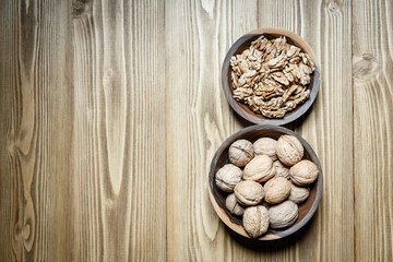 Peeled walnuts and nuts in a  shell in walnut wooden bowl on a wooden background.