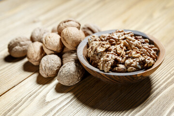 Peeled walnuts and nuts in a  shell in walnut wooden bowl on a wooden background.