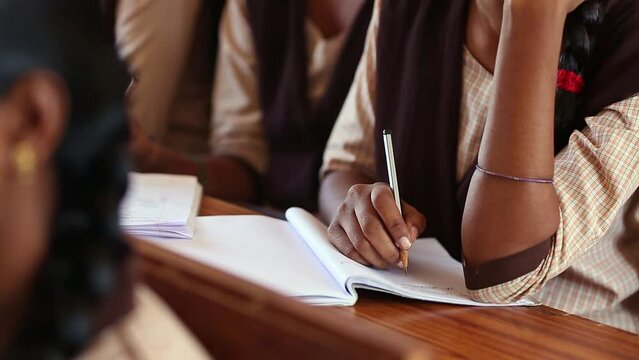 Female student hand writing in notebook on desk with pencil
