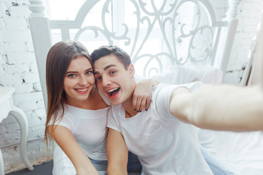 Young cheerful couple taking selfie pictures with a smart phone in bedroom. Celebrating Saint Valentine's day together.