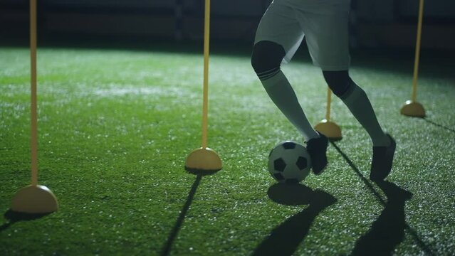 physical exercise in football training, black man running with ball between sticks, closeup of legs