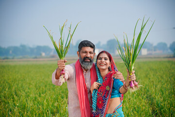 Indian farmer couple holding onion crop in hand at agriculture field. - obrazy, fototapety, plakaty