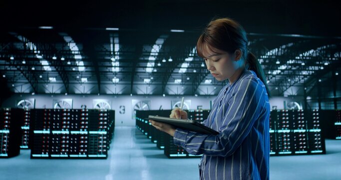A Young Female Using Tablet While Working in Server Room in Contemporary Data Center. IT Technician. Cloud Storage Technology, Database, Engineering. - Powered by Adobe