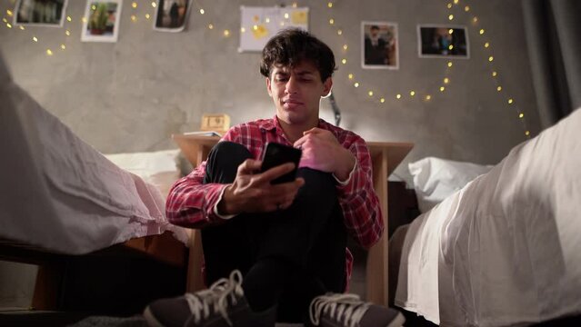 one sad teen student is holding a mobile phone while depressed sitting on the floor in a college dorm. The concept of bullying, discrimination and racism and bullying.