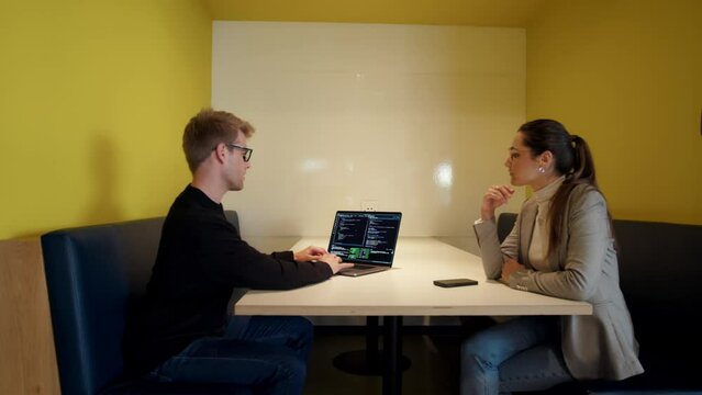 Programmers having a discussion while coding on a laptop in an office. Two software engineers collaborating on a project. Young business people working in tech.