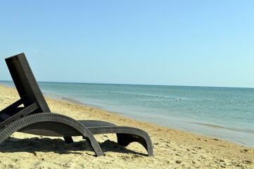 There is a brown chaise longue on the sandy beach by the sea.