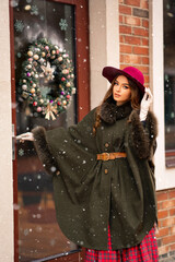 Elegant lady in vintage coat, red checkered dress and hat on Christmas background.Beautiful model in winter snowy art pictures. Luxurly girl in holiday mood.