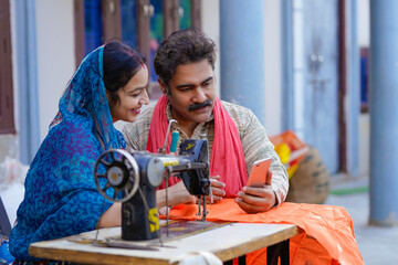 Rural indian man and woman using sewing machine and watching detail in smartphone.
