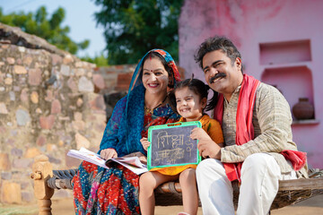 education concept : Indian rural couple showing shiksha words in hindi calligraphy with daughter