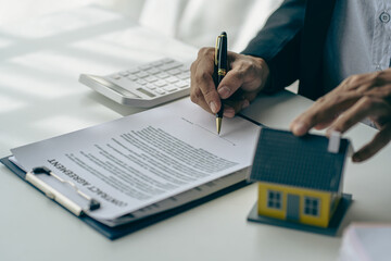 Real estate office, home sales agent sitting at desk with contract documents and house plans next to sale and rental concept.