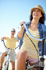 Cycling, travel and couple with a woman on summer vacation or holiday riding on the promenade by...
