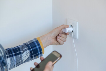 Closeup of a person holding a smartphone and a charger to put it on charge. Horizontal image and copy space.