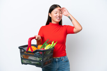 Obraz na płótnie Canvas Young Asian woman holding a shopping basket full of food isolated on white background smiling a lot