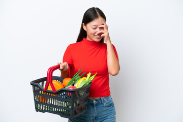 Young Asian woman holding a shopping basket full of food isolated on white background laughing