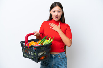 Young Asian woman holding a shopping basket full of food isolated on white background surprised and shocked while looking right