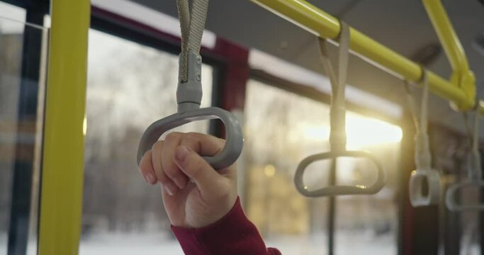 Close up of paasanger holding handle on bus. Man wearing sprty clothes traveling, having trip, going home after work at evening, sunset. Concet of transport and urban lifestyle.