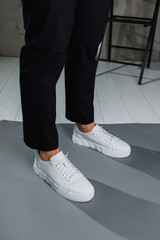 Close up of male legs in black pants and white casual sneakers. Men's leather summer shoes