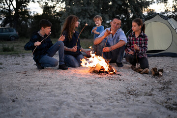 Family grilling marshmallows in the evening on beach.