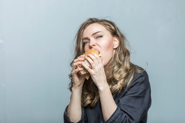A young woman eats a hamburger with appetite. fast junk delicious food. Grey background. Close-up.